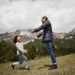 A mother and child embrace joyfully in a lush mountain setting, capturing a moment of happiness and love.
